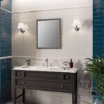 Bathroom vanity with dark wood cabinet, white marble countertop, single sink, framed mirror, teal tiled walls, and two wall sconces.